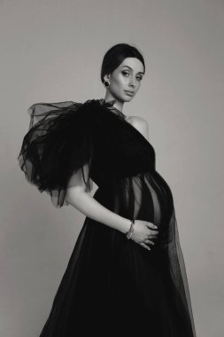 Stüdyoda poz veren, koyu renk saçlı, gece giysili, güzel hamile bir kadının moda fotoğrafı.