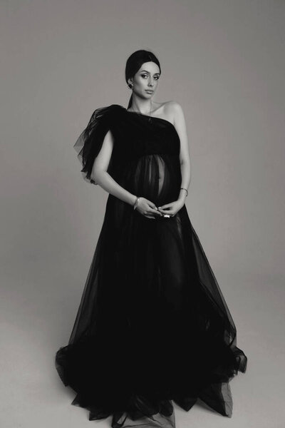 Интерьер моды фото красивой беременной женщины с темными волосами в роскошном вечернем тюле черного платья позирует в студии