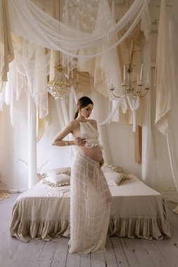 Zarif yatak odasında poz veren siyah saçlı güzel hamile Slav bir kadının moda fotoğrafı.