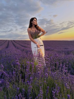 Gün batımında lavanta çiçekli sahada aksesuarlarla poz veren siyah saçlı güzel bir kadının açık hava fotoğrafı.