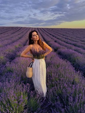 Gün batımında lavanta çiçekli sahada aksesuarlarla poz veren siyah saçlı güzel bir kadının açık hava fotoğrafı.