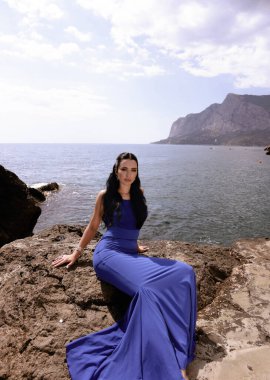 Sahilde poz veren siyah saçlı, zarif mavi elbiseli güzel bir kadının moda fotoğrafı.