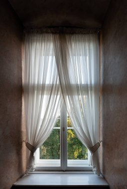 Bahçeye bakan, yarı şeffaf perdelerle kaplı bir pencere. 