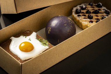 Üç sıra dışı kek, karton bir kutuda kızarmış yumurta, tutkulu meyve ve kuşüzümü turtası ile sandviçe benziyor..