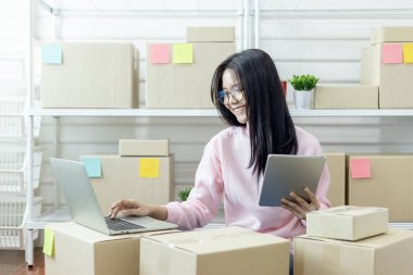Genç Asyalı kadın dizüstü bilgisayar kullanarak ürün satın alma siparişlerini kontrol ediyor ve müşterilere teslimat için paket hazırlıyor. İnternetten ürün satıyorum. İnternetten alışveriş. İnternet işi. Küçük işletme girişimcisi KOBİ 'nin fikirlerini çevrimiçi başlatıyorum. Çalış