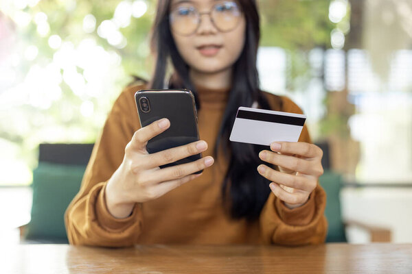 Asian woman holding smartphone and credit card  to shopping online and paying her order