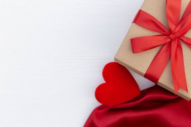 Hediye kutusu ve beyaz ahşap arka planda kırmızı saten. Kırmızı kurdele. Sevgililer Günü hediyesi..