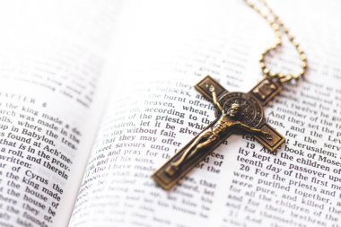 A bronze crucifix necklace placed on an open Bible, symbolizing Christian devotion, the crucifixion of Jesus Christ, and spiritual reflection through scripture.