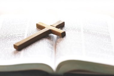 Açık bir İncil 'in üzerinde duran ahşap bir haç, yumuşak doğal ışıkla yıkanmış, Hristiyan inancını, kutsal kitabı ve ruhani yansımasını simgeliyor..