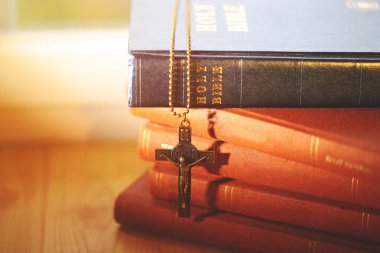 A crucifix necklace hanging on stacked Holy Bibles, illuminated by soft sunlight, symbolizing Christian faith, devotion, and the sacred power of scripture.