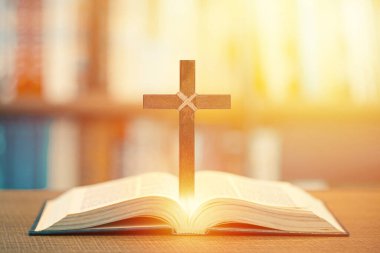 Ahşap Hıristiyan haçı, parlak güneş ışığıyla açık İncil 'in üzerinde duruyor.