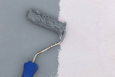Beyaz duvara gri boya uygulayan mavi saplı boya silindiri, yenileme ve ev dekorasyonu kavramı.