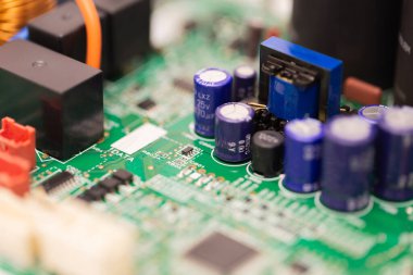 Mavi kondansatörleri, transistörleri ve mikro elektronik bileşenleri gösteren yeşil bir devre kartının makro görüntüsü. Görüntü modern elektronik teknoloji ve donanım mühendisliğini vurguluyor.