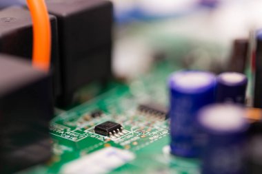 Elektronik cihazlar ve otomasyon sistemlerinde kullanılan anahtar bileşenleri gösteren yeşil baskılı devre kartına monte edilmiş küçük bir mikroçip ve çevreleyen kapasitörlerin yakın görüntüsü.