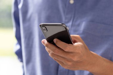 Akıllı telefonu elinde tutan adamın yakın çekimi, günlük mavi gömlek, modern yaşam tarzı ve iletişim konsepti..