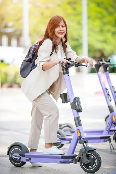 穿着西服的时髦女士骑电动车沿着办公楼上班 — 图库照片