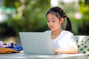 Küçük Asyalı kız okulda öğrenmek için dizüstü bilgisayar kullanıyor. Çocuk mutlu bir şekilde gülümser ve uzaktan bilgi alır. Bu da sınıfın öğrenme becerisini arttırır. Okula Dönüş Konsepti.