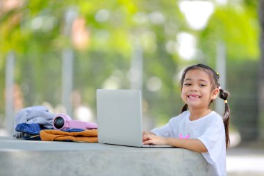 Küçük Asyalı kız okulda öğrenmek için dizüstü bilgisayar kullanıyor. Çocuk mutlu bir şekilde gülümser ve uzaktan bilgi alır. Bu da sınıfın öğrenme becerisini arttırır. Okula Dönüş Konsepti.