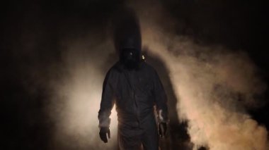 Biyolojik tehlike taşıyan kimyasal koruyucu kıyafet giyen ve karanlık arka planda maske takan bir adam.