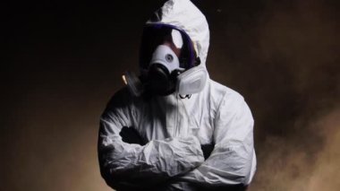Biyolojik tehlike taşıyan kimyasal koruyucu kıyafet giyen ve karanlık arka planda maske takan bir adam.