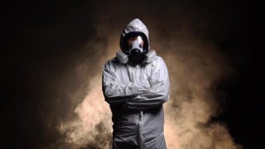Biyolojik tehlike taşıyan kimyasal koruyucu kıyafet giyen ve karanlık arka planda maske takan bir adam.
