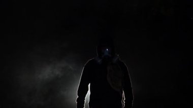 Biyolojik tehlike taşıyan kimyasal koruyucu kıyafet giyen ve karanlık arka planda maske takan bir adam.