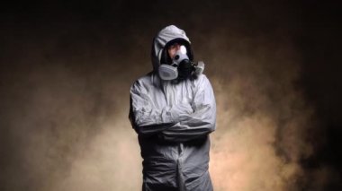 Biyolojik tehlike taşıyan kimyasal koruyucu kıyafet giyen ve karanlık arka planda maske takan bir adam.