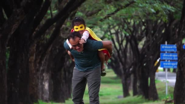 アジアの父遊びとともに彼の小さな娘身に着けているスーパーヒーロー衣装で公園 — ストック動画