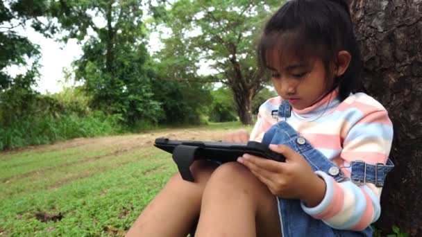 亚洲小女孩坐在公园里学习和使用平板电脑 — 图库视频影像