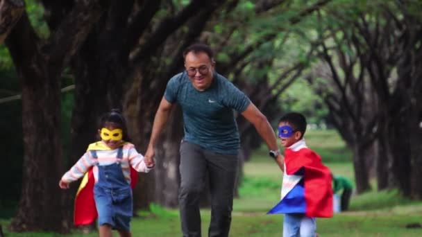 Asiatisk Far Leker Med Sina Små Barn Superhjältedräkter Parken — Stockvideo