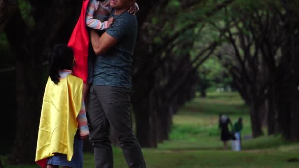 Азіатський Батько Грається Своїми Маленькими Дітьми Костюмах Супергероя Парку — стокове відео
