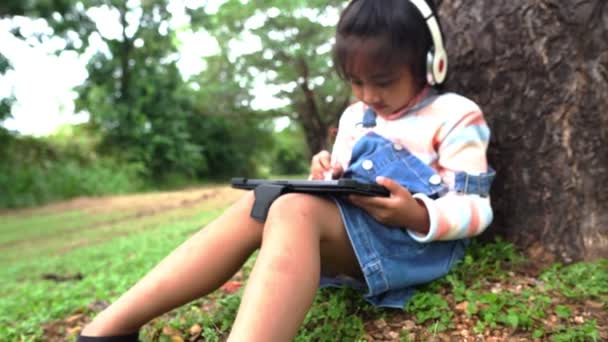 亚洲小女孩坐在公园里学习和使用平板电脑 — 图库视频影像