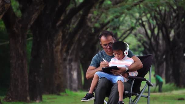 Ασιάτης Πατέρας Και Γιος Κάθονται Στο Πάρκο Σπουδάζοντας — Αρχείο Βίντεο