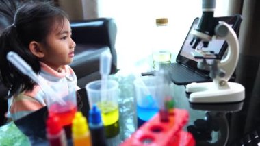 Asyalı küçük kız sıvı ve mikroskopla fen laboratuarı deneyi yapıyor.