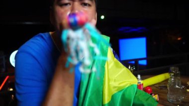 Karnaval düdüğü çalan heyecanlı adam evde TV seyrediyor.