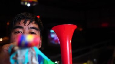 Karnaval düdüğü çalan heyecanlı adam evde TV seyrediyor.