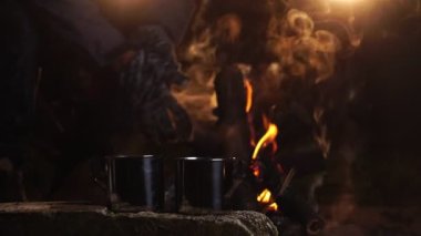 Geceleri kamp ateşinin yanında sıcak içecek dolu metal bardaklar. 