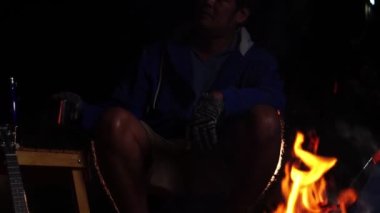  Geceleri ormanda kamp ateşinin yanında ukulele oynayan bir adam. Seyahat ve eğlence. 