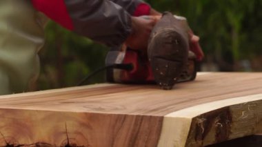 Male carpenter is using electric woodworking tool to work outdoors