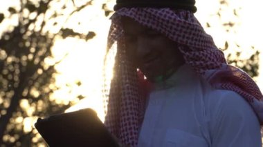 Arab businessman wearing national dress using tablet technology at sunset