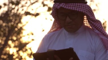Arab businessman wearing national dress using tablet technology at sunset