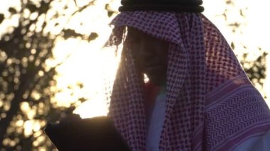 Arab businessman wearing national dress using tablet technology at sunset