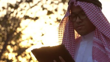 Arab businessman wearing national dress using tablet technology at sunset