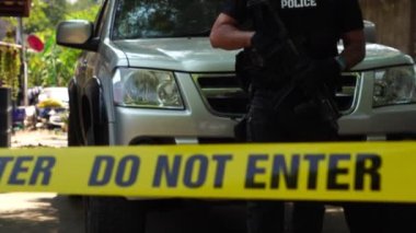 close-up footage of do not enter ribbon in front of vehicle at place of crime while policeman walking around