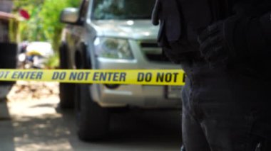 close-up footage of do not enter ribbon in front of vehicle at place of crime while policeman walking around