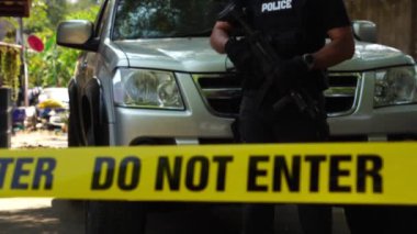 close-up footage of do not enter ribbon in front of vehicle at place of crime while policeman walking around