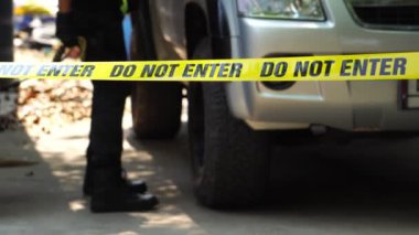 close-up footage of do not enter ribbon in front of vehicle at place of crime while policeman walking around with dog