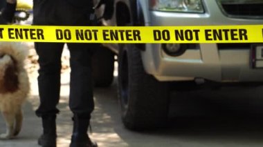close-up footage of do not enter ribbon in front of vehicle at place of crime while policeman walking around with dog