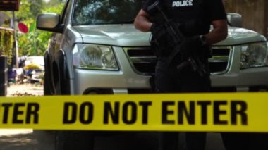 close-up footage of do not enter ribbon in front of vehicle at place of crime while policeman walking around