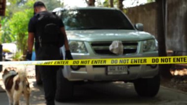 close-up footage of do not enter ribbon in front of vehicle at place of crime while policeman walking around with dog